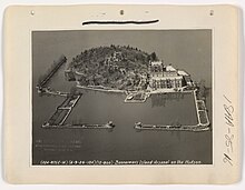 Island with castle, and rectangular man-made harbor encloses the dock. Large lettered signage for "Bannerman's Island Arsenal" runs across the top of the castle exterior below the crenellations.