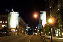 Illuminated buildings line a wide one-way city  street at night