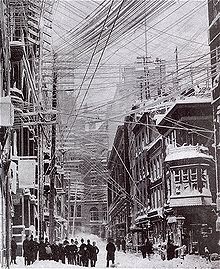 The myriad of telephone, telegraph, and power lines over the streets of New York City in a photo of the Great Blizzard of 1888. An AC line that fell during the storm led to the electrocution of a boy that spring. Blizzard 1888 01.jpg