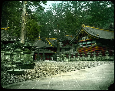 Group of buildings set among trees; ornamental stone wall in front