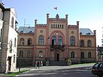 Town hall of Kuldiga, a building with gabled roof with a facade painted in red and brown, and with a flag of Latvia the top of the building