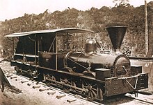 An old photograph showing a shiny black locomotive having a cab with open sides and a large, funnel-shaped smokestack