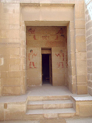 Rear wall of a vestibule in the tomb is visible through a doorway. On this wall, above and to the sides of a second door leading farther into the tomb, are murals painted in color. They show Khnumhotep and Niankhkhum seated at table above the second door, then they stand facing one another across the second door, each holding his staff of authority.