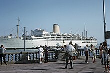 A passenger line at dock with pedestrians on the quay