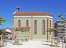 Petit et étroit bâtiment religieux vert orné de brique rouge et pierre blanche surmonté d'un clocheton.