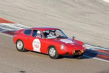 Photo d'une petite voiture de course rouge sur un circuit, avec le capot moteur arrière légèrement ouvert