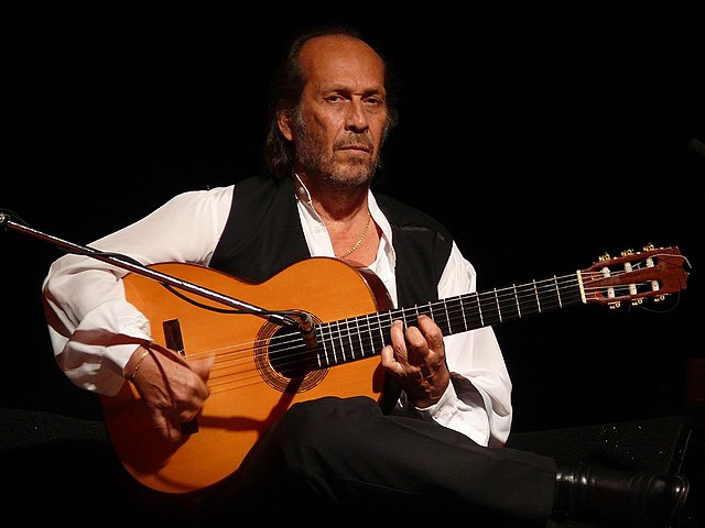 Photographie d'un homme assis sur scène, jouant de la guitare