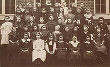 Photographie scolaire en noir et blanc d'une classe de filles avec leur institutrice.