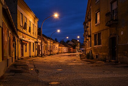 Noite em Esztergom, Hungria — rua Simor János. Esztergom é uma cidade industrial, escolar e portuária situada na margem direita do rio Danúbio. A cidade no sentido atual foi criada em 1895 pela fusão da cidade real livre de Esztergom e de assentamentos vizinhos. Desde a queda da República Popular da Hungria em 1989, até 2012, foi sede do Tribunal Constitucional, e a partir de 1997, sede do Parque Nacional Danúbio-Ipoly. É o centro da Igreja Católica Romana na Hungria, e um destino turístico popular, escolhido por um milhão e meio de turistas em 2014. (definição 3 387 × 2 294)