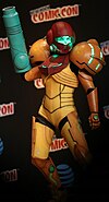 Samus Aran, héroïne des trois jeux de la série Metroid Prime (cosplay, femme dans un costume de Samus Aran de couleur jaune et rouge.