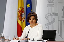 Photographie d'une femme, assise à un bureau vêtue de blanc.