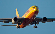 Cropped photo of a yellow and red 767 preparing to land. Undercarriage are extended. One engine is hung beneath each of the two wings.