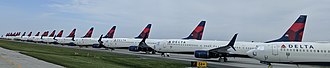 Много в редица самолети с логото на Delta Air Lines на опашката, паркирани на настилка зад ограда.