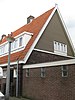 Blok met 8 keukenwoningen, zo genoemd vanwege destijds nieuwe plaatsing van keuken aan de voorzijde, aan de zijkant een houten topgevel, bouwstijl Amsterdamse School, samen met de poortgebouw langs de Purmerweg centraal deel van Tuindorp Nieuwendam