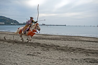 Mounted archer rides on beach.