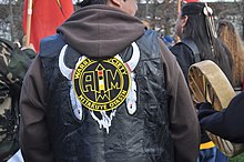 A participant at the raising of the John T. Williams Memorial Totem Pole in Seattle wears the AIM colors on their jacket, February 26, 2012 American Indian Movement Jacket.jpg