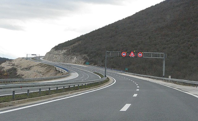 Variable traffic signs placed on a gantry indicating speed limit for each traffic lane and slippery road surface warning.