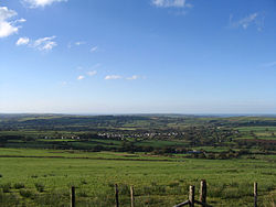 small village in a valley surrounded by green fields with the sea visible in the background