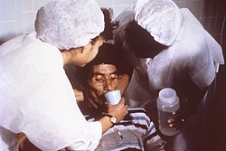 Nurses encouraging this patient to drink an Oral Rehydration Solution to improve dehydration he acquired from cholera.