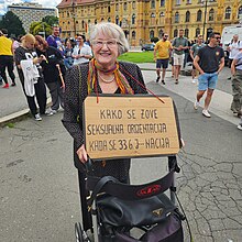Older female activist on Zagreb Pride 2024 with a banner with an intersectional question: What is sexual orientation term used for nation being f___ed for 33 years?