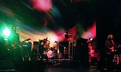 A rock band performing live on stage against a green and red backdrop.