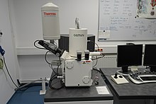 A photograph of an electron microscope consisting of three white modules sitting on a desk