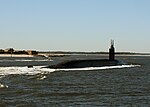 Three quarters view of submarine running on surface near land.