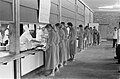 Une longue file de femmes en robe longue attendent d'être servies à une cantine.