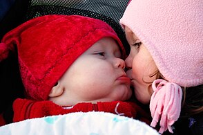 Una nena li fa un petó a un bebè a la galta.