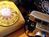 דוגמאות לטכנולוגיות בולטות משנות ה-60 – מכשירי טלפון חוגה בעיצוב הסטנדרטי בעשור זה, ומצלמת קודאק.