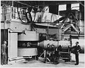 Foto en blanco y negro de maquinaria pesada con dos operadores sentados a un lado.