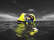 An EPIRB floating in the water next to distressed boating family in a liferaft