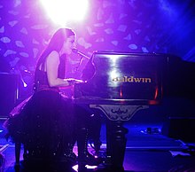 Молодая женщина с длинными темными волосами поет и играет на фортепиано на сцене