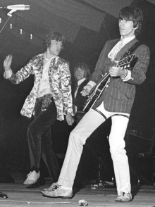 Black and white photo of three men performing on a stage, two of them in the foreground and one behind them