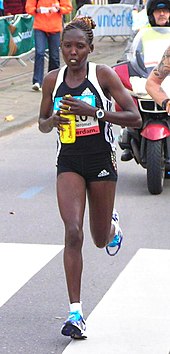 Photo of Lydia Cheromei running on the street and holding a drinking bottle with both hands