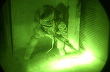 A US soldier in Aksabah, Iraq, uses a pistol-grip shotgun to breach a locked door in a night operation Breaching Door.jpg