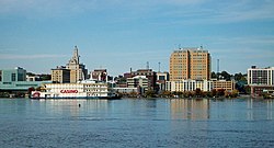 A row of tall buildings in the middle, with a river on the bottom and a blue cloudy sky on top