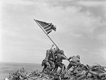 alt = A black-and-white photograph of six American soldiers raising the American Flag.