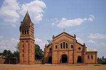 Фотографија која приказује римокатоличку жупну цркву у Руамагани, у Источној провинцији, укључујући главни улаз, фасаду, засебни звоник и земљано предворје.