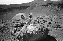 Два человека в одежде космонавтов рядом с глубоким кратером