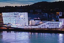 Ars Electronica Center, mehrstöckiges Doppelgebäude mit einer Verbindungsbrücke und Glassfassade, im Bild mit blau-lilaner Beleuchtung