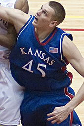 A Caucasian basketball player in a Kansas #45 jersey is boxing out.