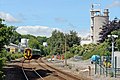 An Arriva Trains Wales Class 158 leaves the station heading north, away from the camera, towards Ruabon. The Kronospan factory is to the right.