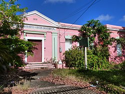 Photograph of the Derkes School, a disused, single-story, pink structure with a classical entry