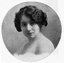 A white woman with short dark wavy hair in a circle frame.