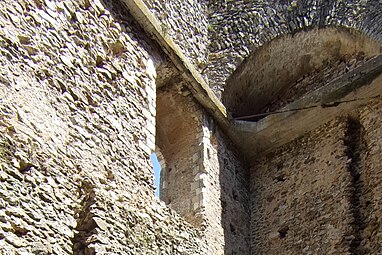 Photographie en couleurs d'un mur pourvu d'un arc en maçonnerie et ceinturé par un bandeau de béton armé.