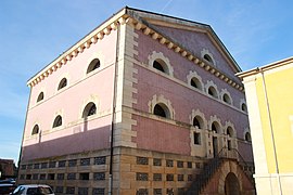 Photographie en couleurs d'un bâtiment à étages en maçonnerie rose éclairé de petites baies en demi-cercle.