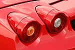 Sarkanās sporta automašīnas detaļa, kas sastāv no diviem apaļiem aizmugurējiem lukturiem
