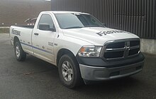 A two-door white pickup truck seen from a three-quarter angle, in slight mist with some brown metallic vertically corrugated warehouse walls in the background