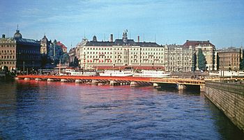 Strömbron under uppförande 1946 och sedd från samma plats år 2010. Bron grundlades provisorisk på träpålar, som sticker upp över vattenytan, vilket framgår på bilden från 1946. I bakgrunden syns Grand Hôtel innan takvåningen påfördes.